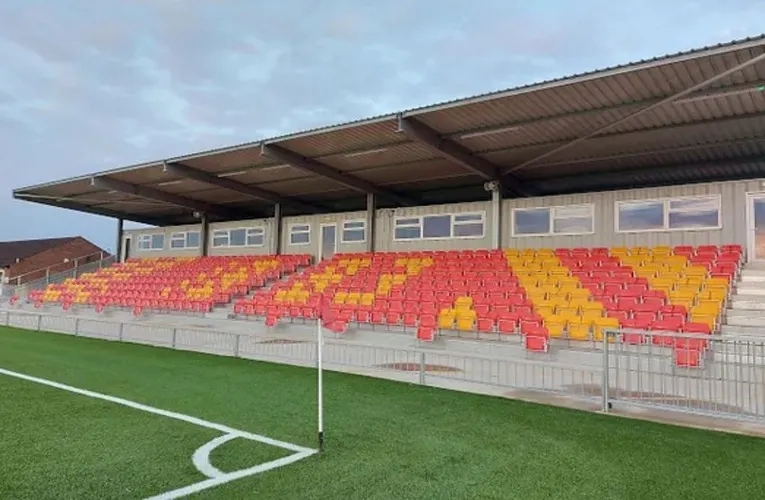 Khán đài có mái che của sân Meadow Park Gloucester với hàng ghế đỏ và trắng nổi bật, nơi cổ động viên hòa mình vào không khí bóng đá Non-League