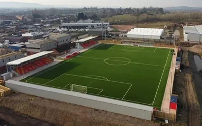 Sân vận động Meadow Park Gloucester nhìn từ xa, với khán đài và sân cỏ nhân tạo Tiger Turf, biểu tượng cho sự kiên cường của bóng đá Anh hậu phương